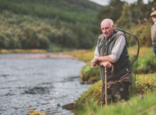 An old man kneels beside a lake in the last keeper