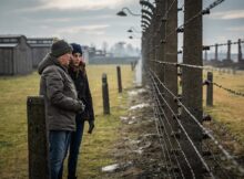 Two people stand in front of barbed wire in For the Living