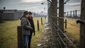 Two people stand in front of barbed wire in For the Living